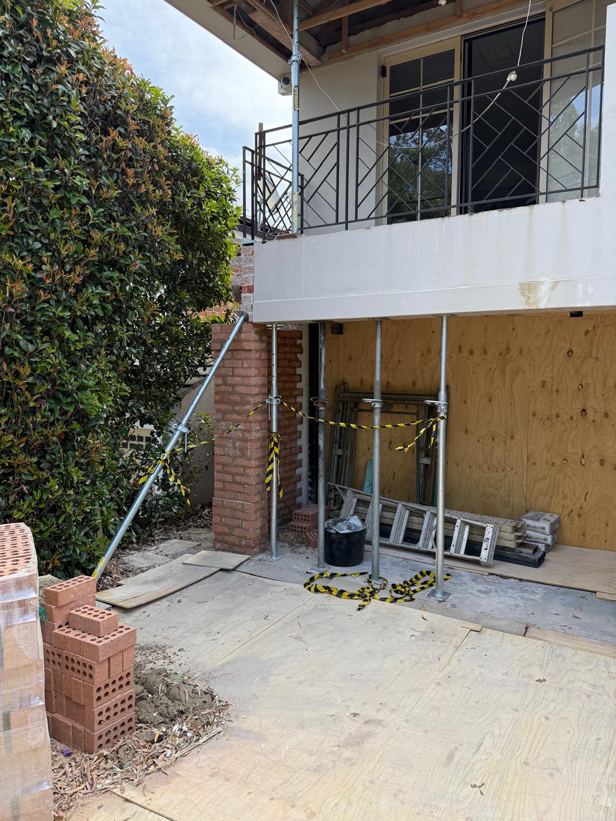 Ground-floor opening propped with acrow props during structural alteration, with new brickwork and ply hoarding