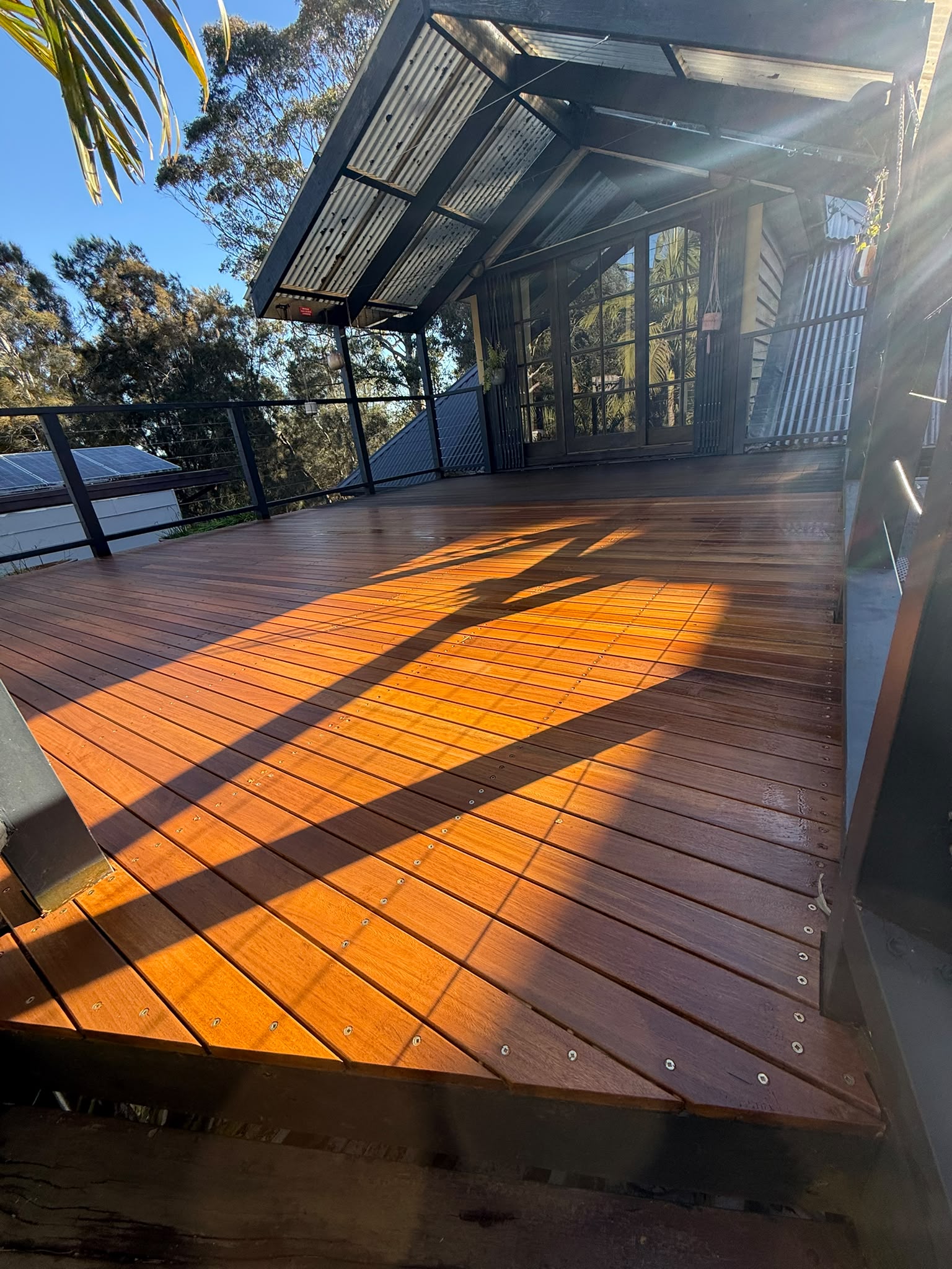 Completed hardwood deck bathed in afternoon sun, with new steel balustrade and covered outdoor area